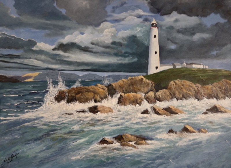 A white lighthouse on a green headland under heavy storm cloud, with waves bursting over the rocks below