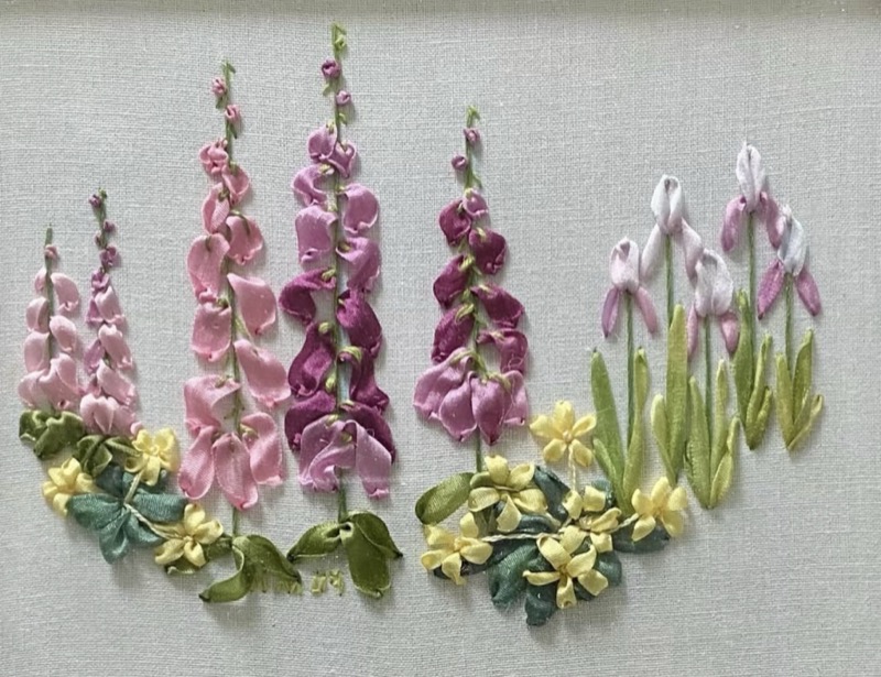 Pink and purple foxgloves in silk ribbon standing beside white and lilac irises, above a bank of small yellow flowers