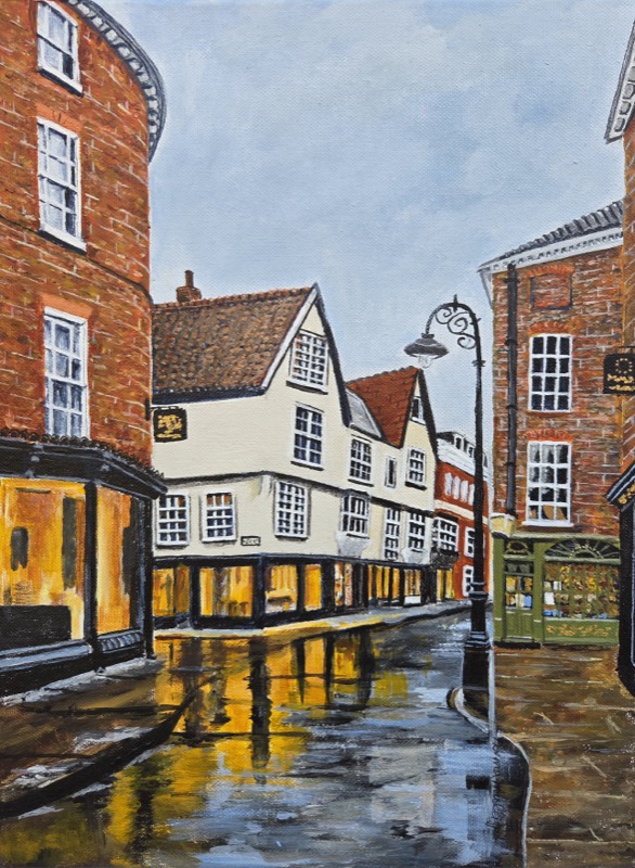 A narrow York street after rain, lit shopfronts reflected in the wet cobbles beneath timbered and red brick buildings
