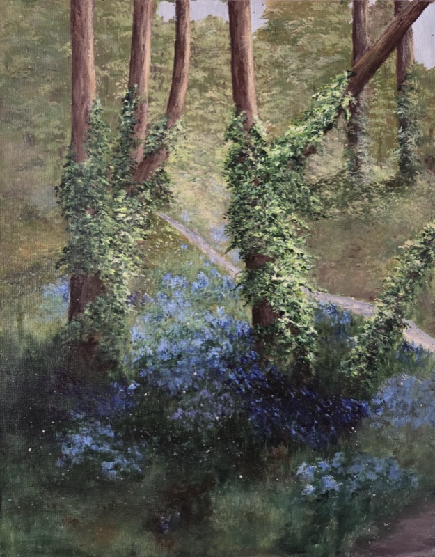 A narrow path running between deep banks of bluebells, past a broad tree trunk wrapped in ivy and moss